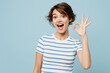 © ViDi Studio - Young happy surprised shocked woman she wears striped t-shirt casual clothes showing okay ok gesture look camera isolated on plain pastel light blue cyan background studio portrait. Lifestyle concept.