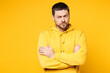© ViDi Studio - Young sad mad frowning dissatisfied Caucasian man he wearing hoody casual clothes hold hands crossed folded look camera isolated on plain yellow orange background studio portrait. Lifestyle concept.