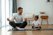 © standret - Lotus pose. Father with little daughter are doing yoga at home