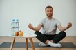 © standret - Bottles of water and apples. Yoga man is sitting on a mat at home
