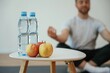 © standret - Focused view on apples and bottles of water. Yoga man is sitting on a mat at home