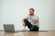 © standret - Man is sitting on the yoga mat with laptop on the floor