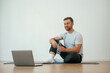 © standret - Man is sitting on the yoga mat with laptop on the floor