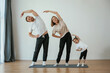 © standret - Warm up exercises. Family of mother, father and daughter are doing yoga at home