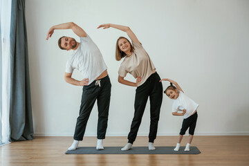 Wall Mural - Warm up exercises. Family of mother, father and daughter are doing yoga at home