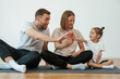 © standret - Doing high five. Family of mother, father and daughter are doing yoga at home