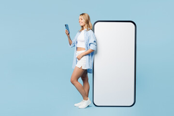 Wall Mural - Full body young happy woman wear white top shirt casual clothes big huge blank screen mobile cell phone with area use smartphone isolated on plain pastel light blue cyan background. Lifestyle concept.