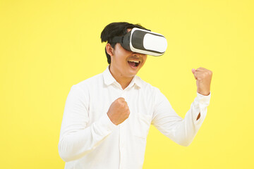 Isolated close up excited man wearing white shirt and VR headset, fist pump gesture, celebrating a win on yellow background