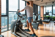 © samael334 - Man working out on an elliptical trainer in modern gym with city view. Male doing cardio training on elliptical machine in fitness studio in residental building. Fitness, wellness, healthy lifestyle