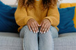 © Nedrofly - Close-up of a woman's hands resting on her lap while sitting on a sofa. She is wearing a yellow knitted sweater and light blue jeans. Concept of waiting, restlessness