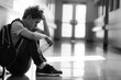 © Alexandra - Sad male student sitting alone on the floor in a school hallway feeling anxious and depressed