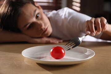 Canvas Print - Eating disorder. Sad woman holding fork with tomato at wooden table indoors, selective focus