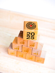 Wall Mural - 2025 business goal and success banner concept. 2025 year numbers with target icon and growth chart symbols on wooden cube blocks pyramid stacked on white vertical background. Happy New Year in 2025.