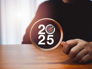 Poster - Happy new year 2025 with business concept banner. 2025 year numbers with target icon in magnifying glass lens, holding by person hand on desk, dark background. Planning for goal and success concepts.