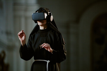 Wall Mural - Medium shot of unrecognizable Catholic nun wearing VR headset standing in cathedral and using AR app, copy space