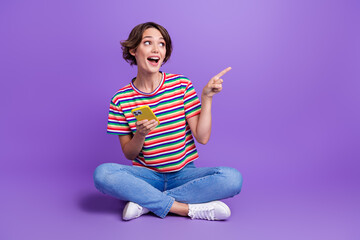 Wall Mural - Photo of excited lovely girl wear trendy clothes sitting floor demonstrating empty space proposition isolated on violet color background