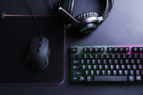 Wired mouse, mousepad, computer keyboard and headset on black table, flat lay