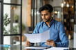 © btiger - Young professional working on laptop and reviewing documents in modern office with glass door