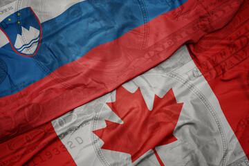 Wall Mural - waving colorful flag of slovenia and national flag of canada on the dollar money background. finance concept.