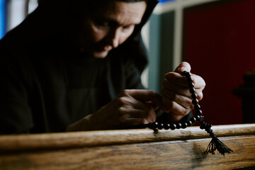 Medium closeup shot of senior Caucasian nun holding beads in hands sitting on pew in church and praying to God