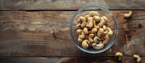 Canvas Print - Top view of a glass bowl filled with raw cashew nuts displayed on a wooden table, creating a serene copy space image.