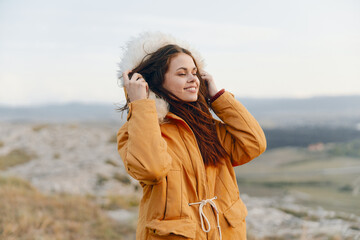 Poster - Alone traveler in yellow coat standing on hill with hands on ears in a peaceful moment