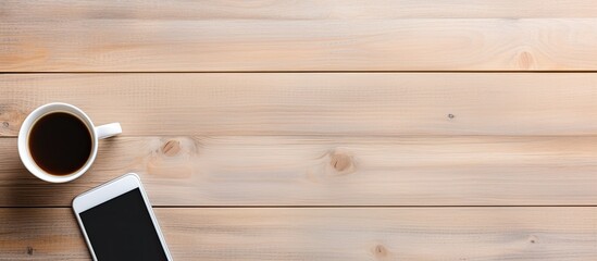 Poster - Aerial view of a wooden desk featuring a blank white smartphone, a coffee cup, a pen, and a spiral notepad with copy space image available.