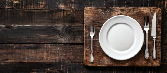 Aufkleber - Top view of an old wooden board with a white plate, fork, and knife on a dark background providing copy space image.