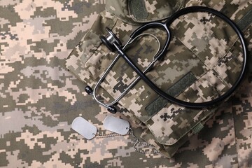 Wall Mural - Stethoscope, military ID tags and soldier uniform on camouflage fabric, flat lay