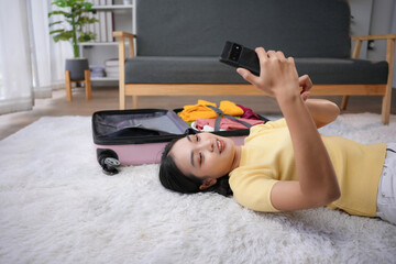 Wall Mural - Young woman lying on floor using smartphone next to packed suitcase