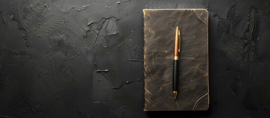 Poster - Top view of a notebook and pen on a black background with ample copy space image.
