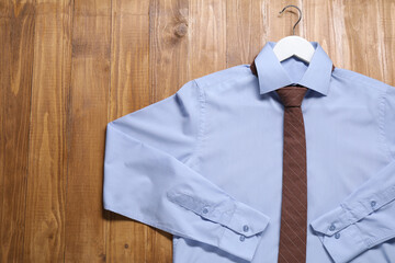 Wall Mural - Hanger with light blue shirt and stylish necktie on wooden background, top view. Space for text