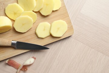 Canvas Print - Fresh raw potatoes, peels and knife on wooden table, top view. Space for text