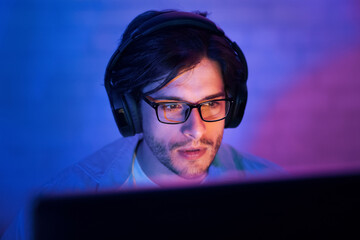 Poster - This image shows a man wearing headphones and glasses, sitting in front of a computer screen. He is focused on the screen, likely engaged in an activity that requires his full attention.