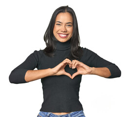 Wall Mural - simple portrait of a young latina smiling and showing a heart shape with hands.