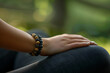 © forenna - closeup photo of an aromatherapy bracelet on a person's wrist, with the person seated in a lotus position in a natural setting. The background features soft-focus greenery and natu