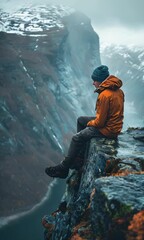 Wall Mural - A man sits on a rock overlooking a river. The man is wearing an orange jacket and a blue hat. The scene is serene and peaceful, with the man taking in the beauty of the landscape