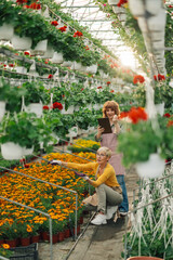 Florist with tablet monitoring and older one is gardening at hothouse