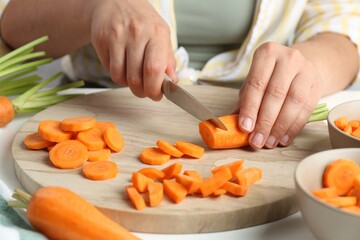 Woman cutting fresh carrot at table, closeup