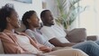 © acnaleksy - african Family sitting together on a couch and watching TV