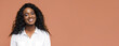 © Prostock-studio - Black woman smiling warmly at the camera. She is wearing a white shirt and her dark curly hair is pulled back from her face. The background is a simple tan color
