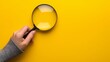 © Alexandra ZH - A hand holding a magnifying glass over a yellow background with copy space, the concept of searching for information or finding a job candidate