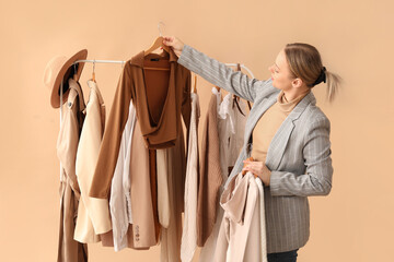 Wall Mural - Female stylist with clothes on rack against beige background