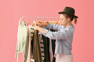 Wall Mural - Female stylist with clothes on rack against pink background