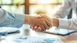 © Nicholas - A close-up shot capturing two individuals shaking hands in a professional setting, with charts and financial documents visible on the table, symbolizing a business agreement.
