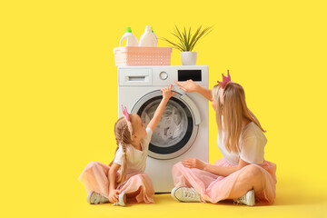 Wall Mural - Happy mother with her little daughter doing laundry on yellow background