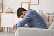 © Pixel-Shot - Tired young man sitting on couch at home