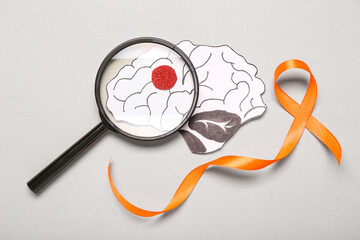 orange ribbon, paper brain and magnifying glass on grey background. multiple sclerosis awareness mon