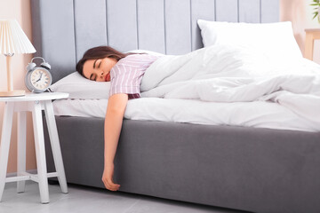 Poster - Pretty young woman sleeping in bed with alarm clock on bedside table