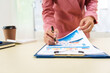 © Phushutter - A businesswoman in a pink suit works at a desk with a whiteboard in the background. She focuses on accounting and financial services, professionalism and expertise in various financial roles.